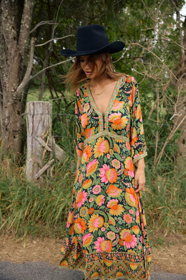 Woman wearing a colorful floral dress and black hat outdoors.