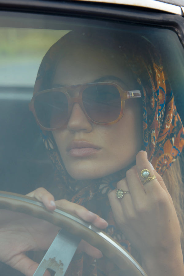 Woman driving a car wearing sunglasses and a patterned headscarf.