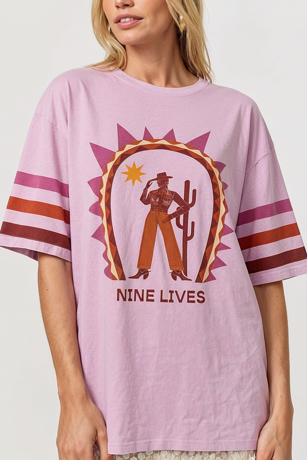 Person wearing a pink t-shirt with a graphic design and 'NINE LIVES' text on a plain background