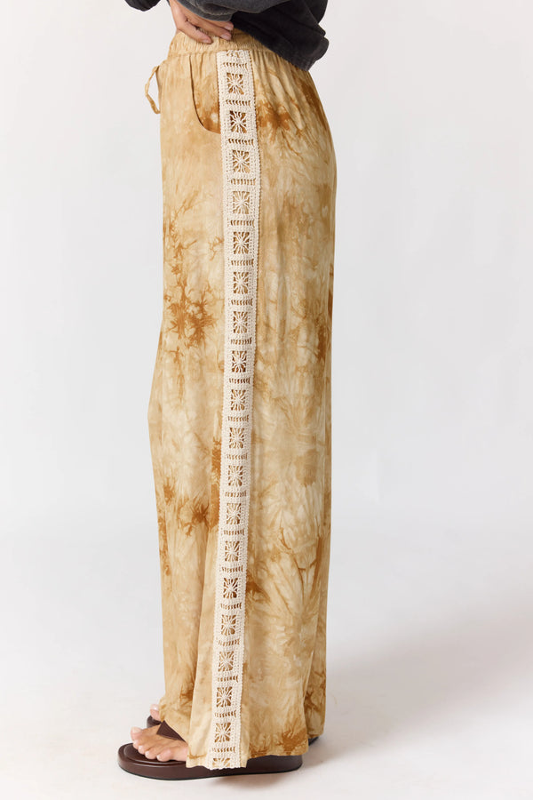 Beige tie-dye pants with a white stripe featuring black text on a white background