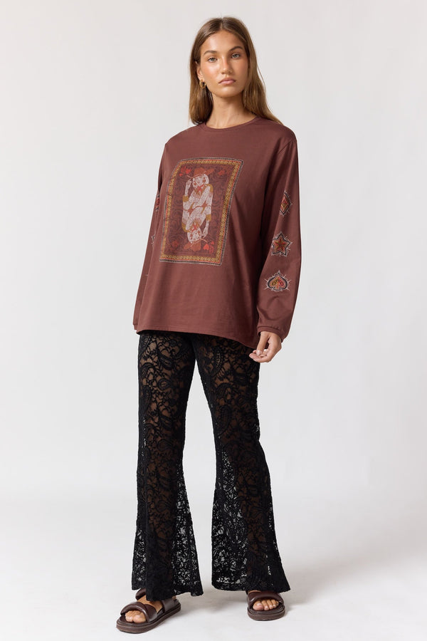 Woman wearing a brown long-sleeve top with a graphic design and black lace pants on a white background