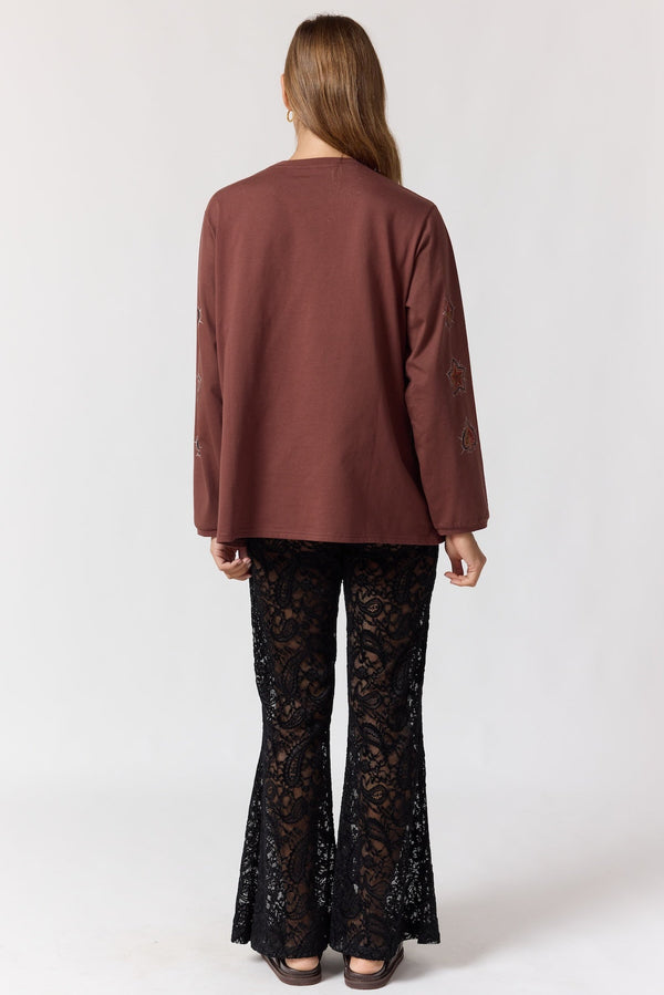 Woman wearing a brown top and black lace pants on a white background