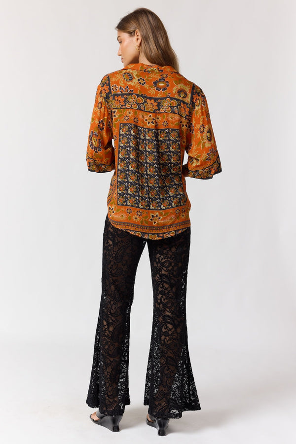 Woman wearing a patterned orange and black blouse with bell sleeves on a white background