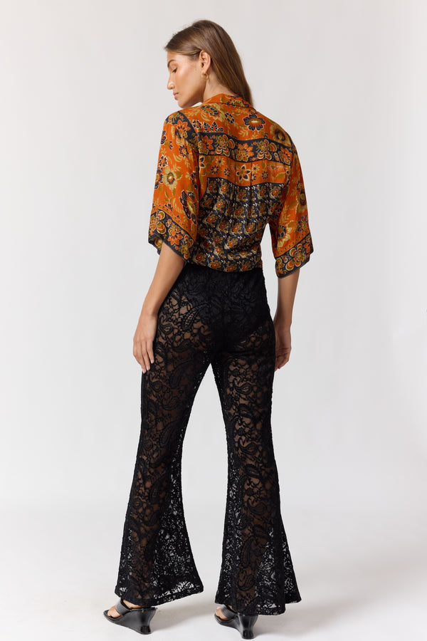 Woman wearing a patterned orange blouse and black lace pants on a white background