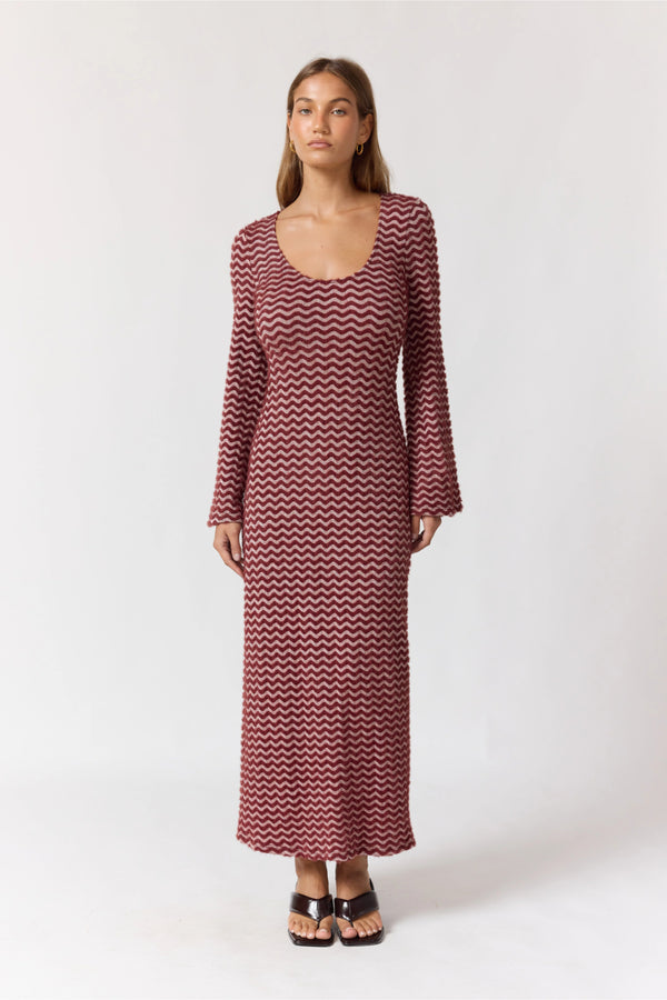 Woman wearing a long burgundy chevron patterned dress on a white background