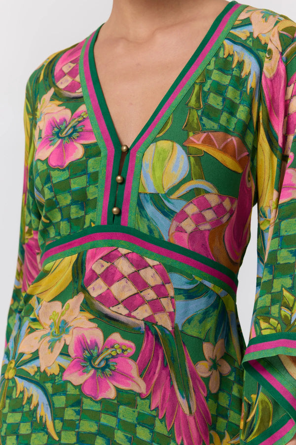 A close-up of a long-sleeve V-neck dress featuring a vibrant tropical print with pink hibiscus flowers, green checkered patterns, and pink and green striped trim.