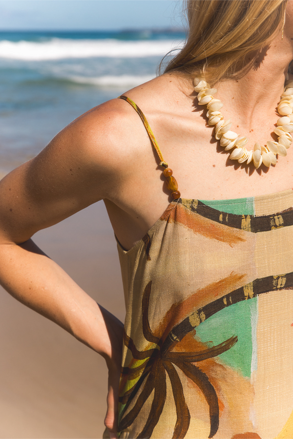 A woman at the beach wearing a beige and brown tropical print camisole top and a shell necklace, with the ocean in the background. Location is Dreamtime Beach, Fingal Heads, NSW.