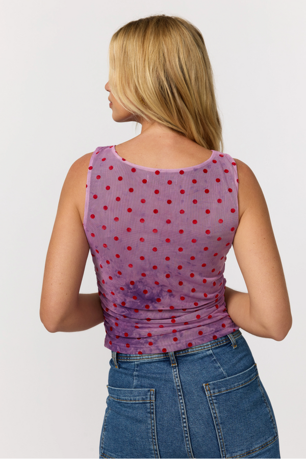 Woman wearing a purple tank top with red polka dots and blue jeans on a white background