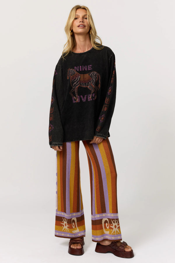 Woman wearing a black sweater with a horse design and colorful patterned pants on a white background