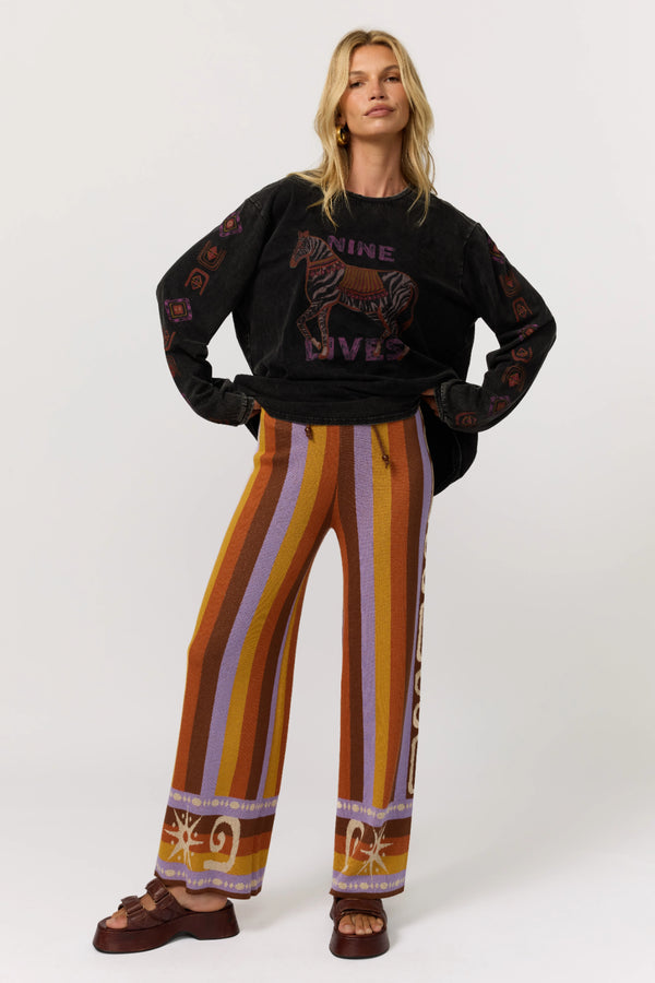 Woman wearing a black sweater with graphic design and colorful striped pants on a white background