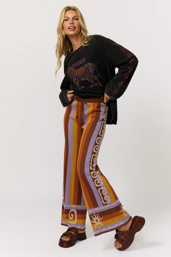 Woman wearing a black sweater with a graphic design and colorful patterned pants on a white background