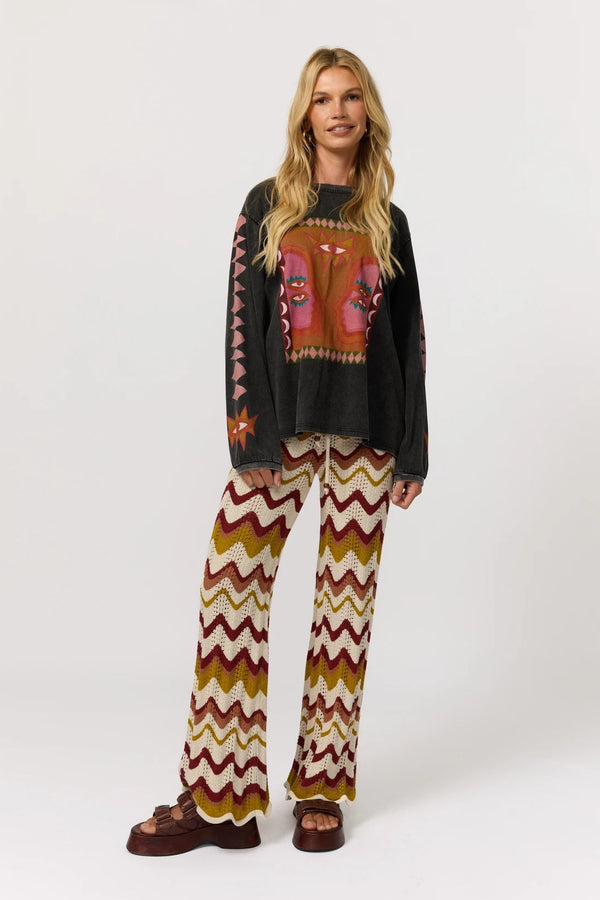 Woman wearing a black sweater with a colorful design and patterned pants on a white background
