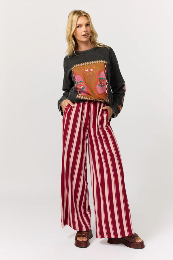Woman wearing a black sweater with a colorful design and red and white striped pants on a white background