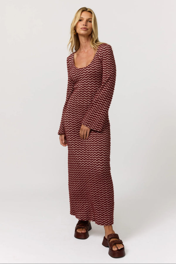 Woman wearing a long burgundy chevron patterned dress on a white background
