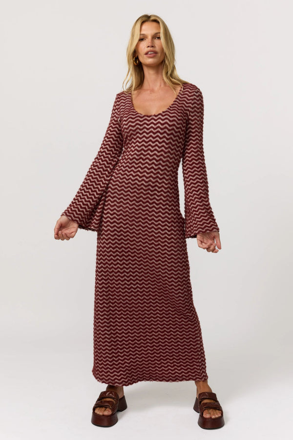 Woman wearing a long burgundy dress with a zigzag pattern on a white background