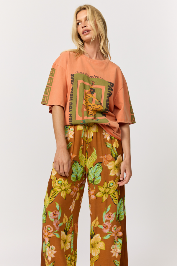 Woman wearing a peach-colored t-shirt with graphic design and brown floral pants on a white background