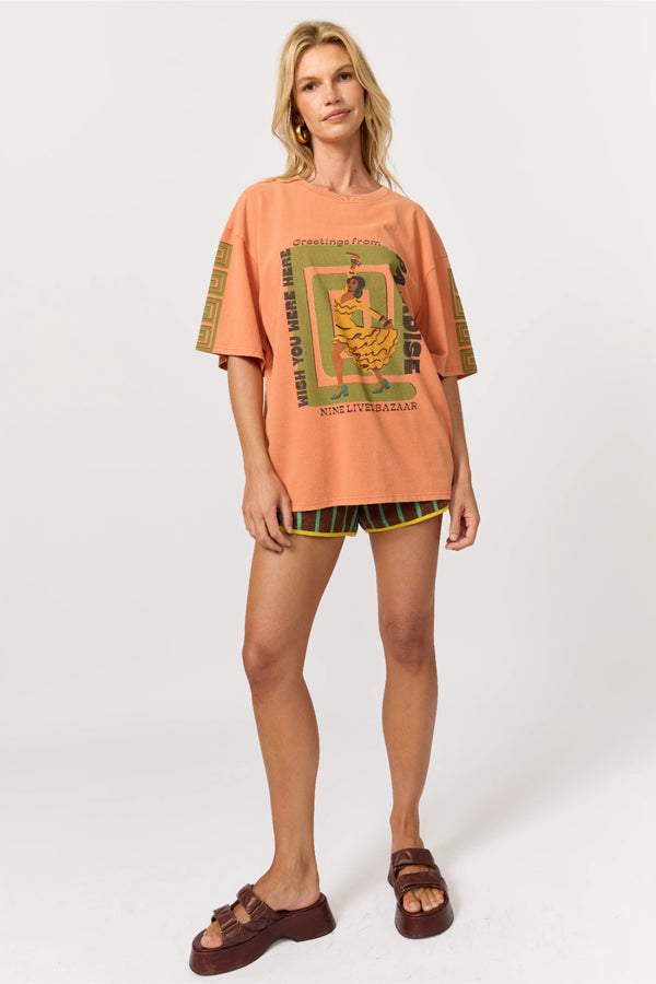Woman wearing an oversized peach t-shirt with graphic design and black shorts on a white background