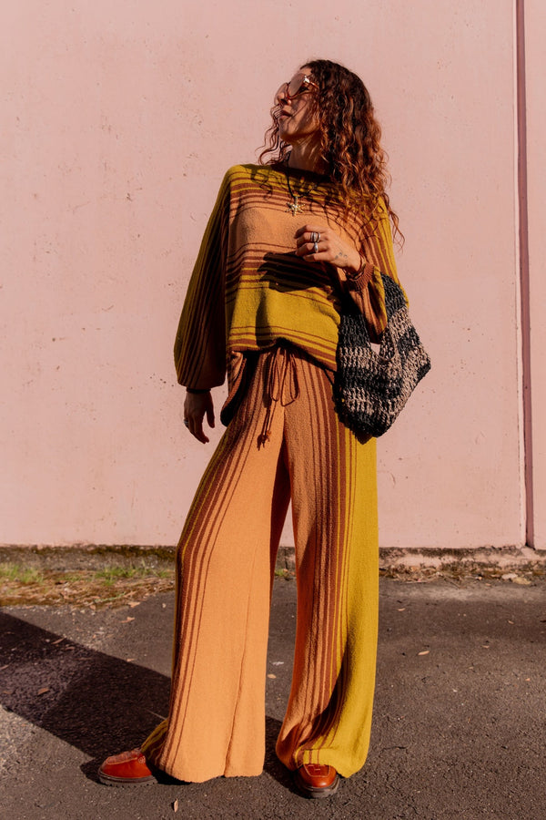 Woman in a mustard yellow and brown outfit standing against a pink wall.