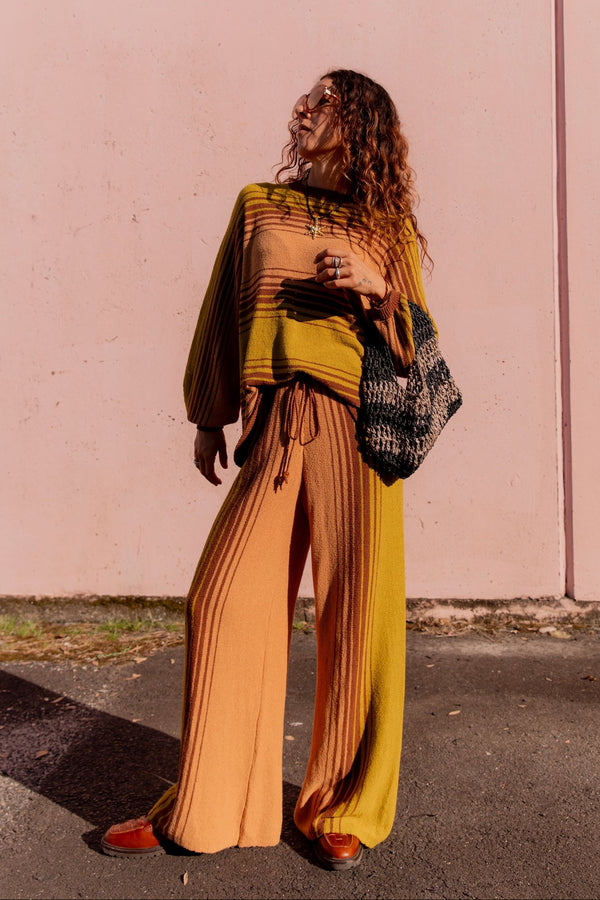 Woman in a mustard yellow and brown outfit standing against a pink wall.