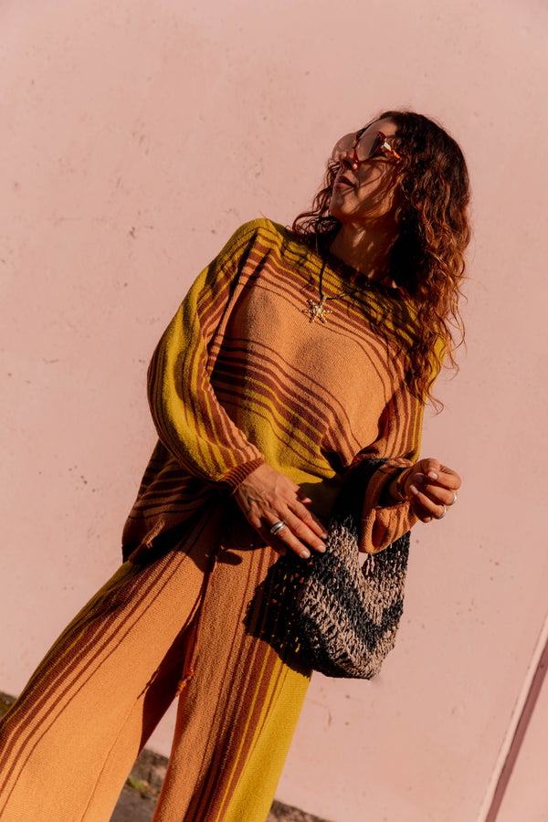 Woman in a mustard yellow outfit holding a textured bag against a pinkish-beige background