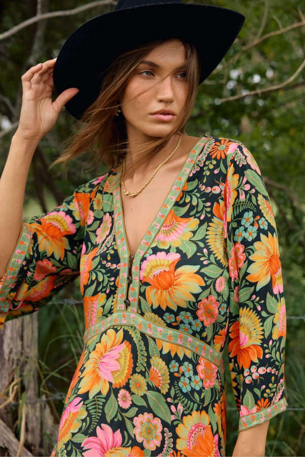 Woman wearing a colorful floral dress and black hat in a natural setting