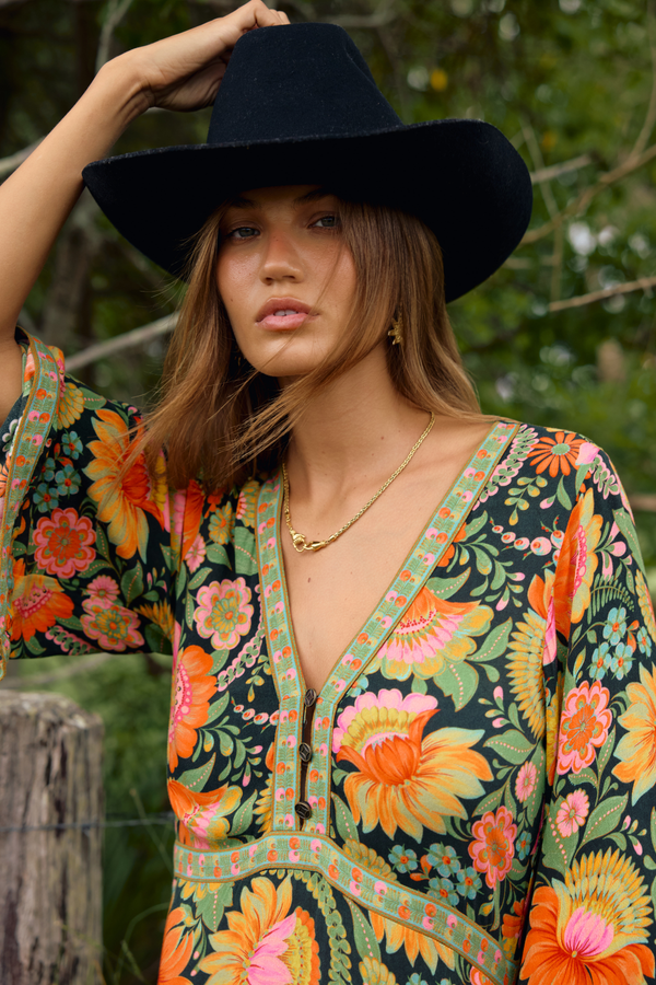 Woman wearing a colorful floral dress and black hat outdoors