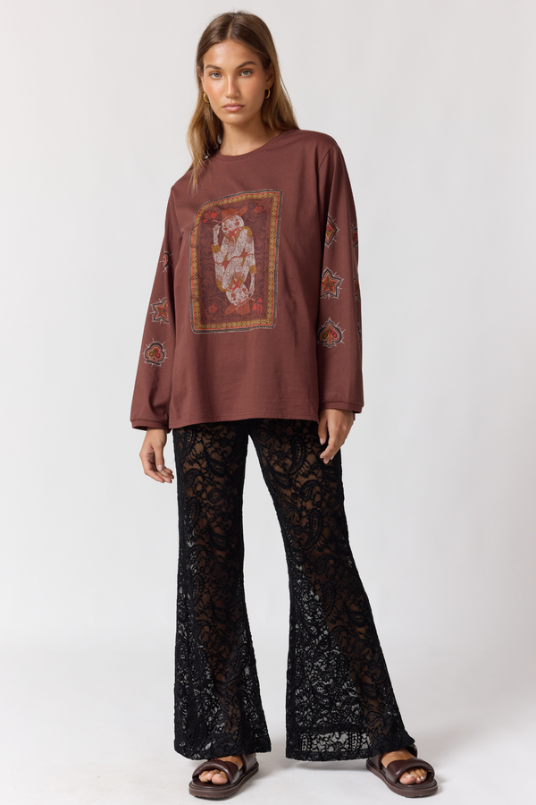 Woman wearing a brown long-sleeve top with a graphic design and black lace pants on a white background