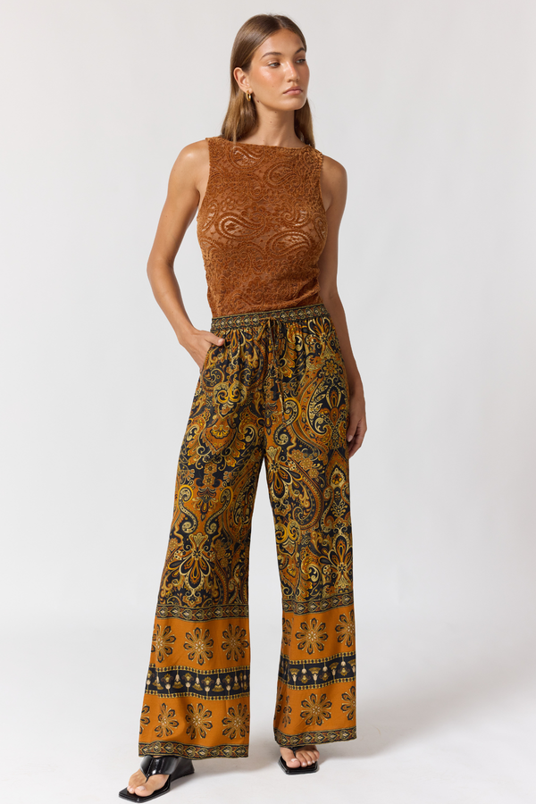 Woman wearing a brown sleeveless top and patterned pants on a white background