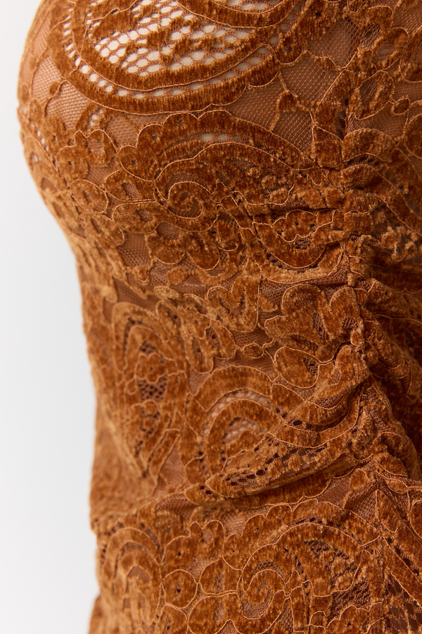 Close-up of brown lace fabric with intricate patterns on a white background