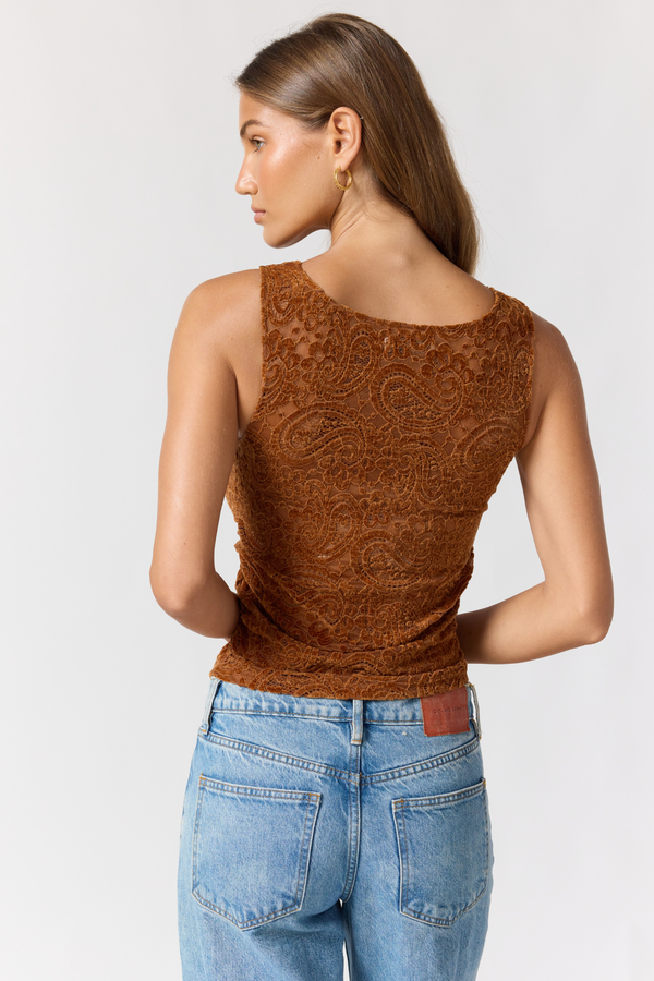 Woman wearing a brown lace top and blue jeans on a white background