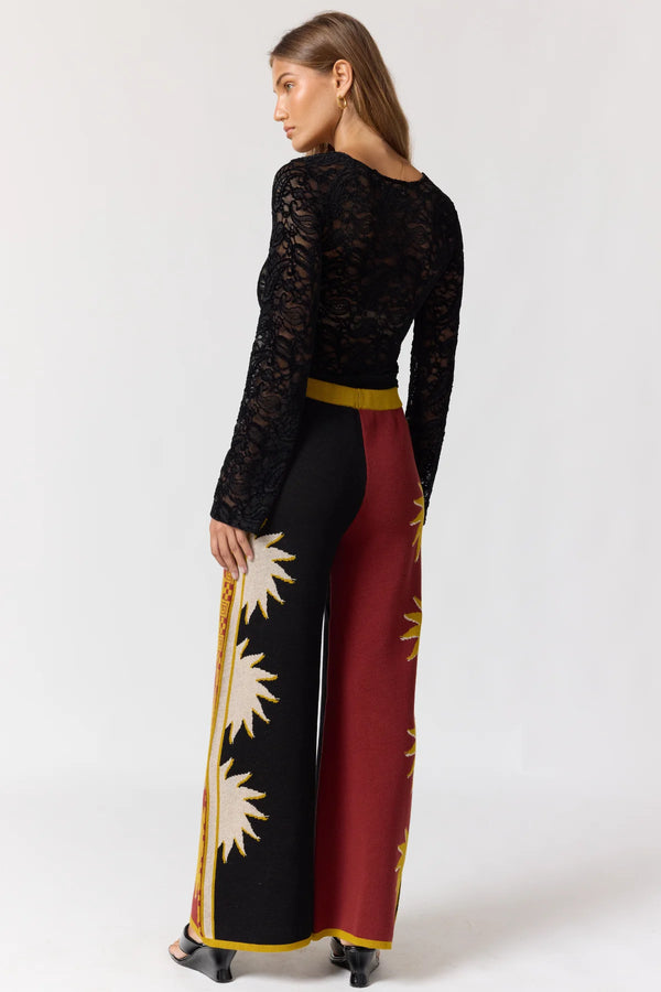 Woman wearing a black lace top and colorful pants with a white background