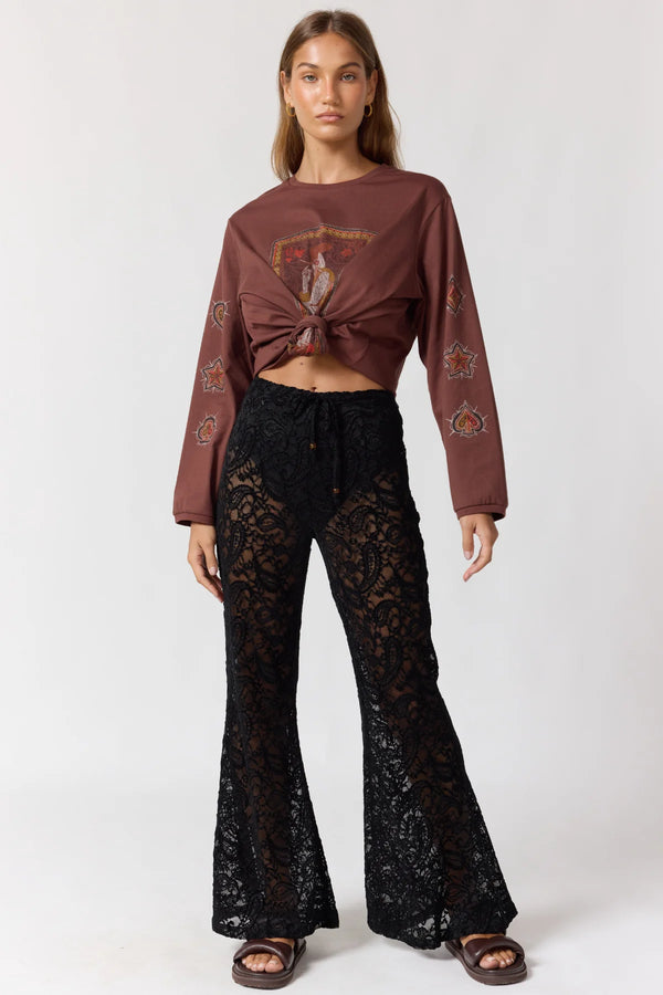 Woman wearing a brown long-sleeve top and black lace pants on a white background