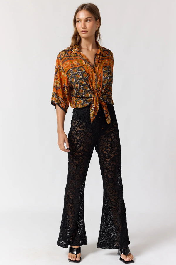 Woman wearing a patterned orange blouse and black lace pants on a white background