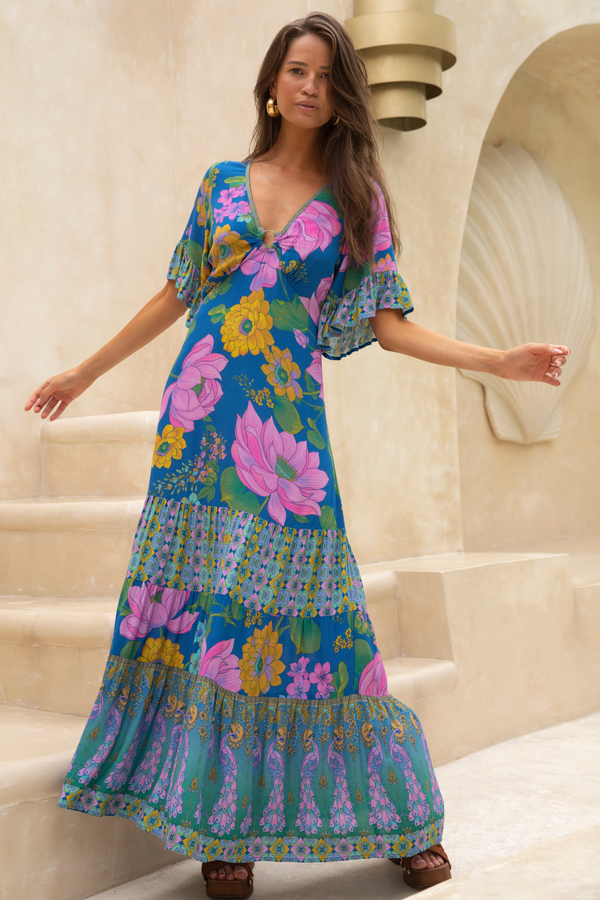 Woman wearing a colorful floral dress standing on steps with a beige wall in the background
