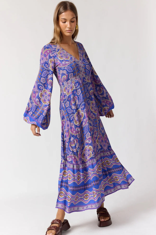Woman wearing a long, patterned dress with bell sleeves on a white background
