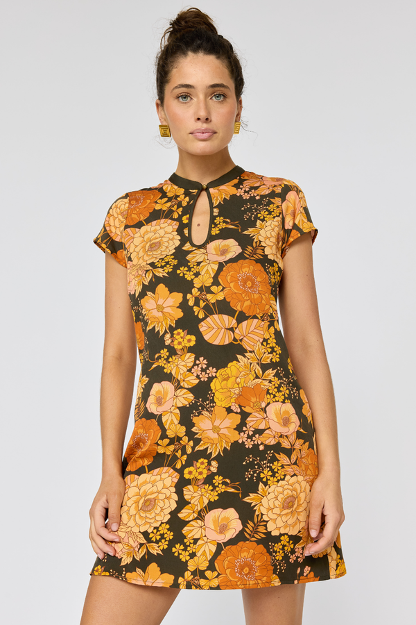 Woman wearing a floral dress with orange and yellow flowers on a plain background