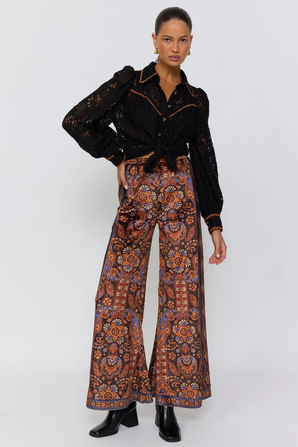 Woman wearing a black patterned shirt and colorful paisley pants on a white background
