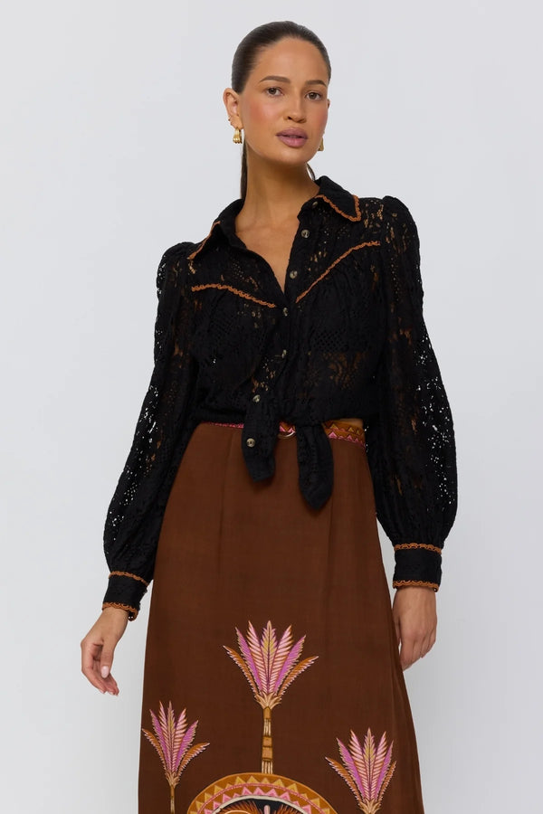 Woman wearing a black embroidered jacket and brown patterned skirt against a white background