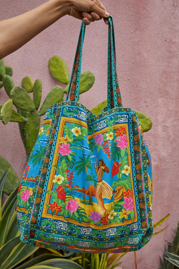 Colorful embroidered bag with tropical design held by a hand against a pink background