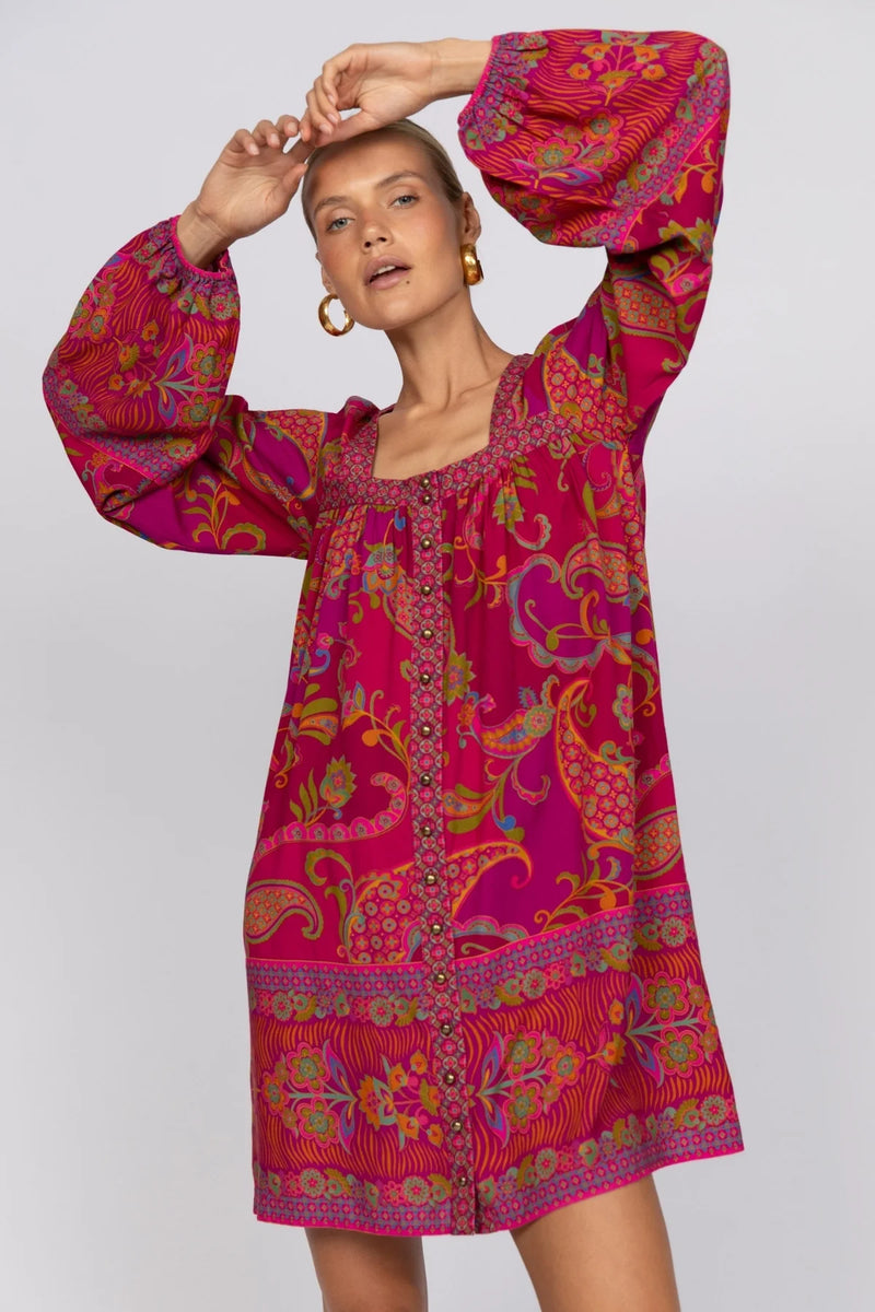 Woman wearing a vibrant pink and red dress with colorful patterns on a white background