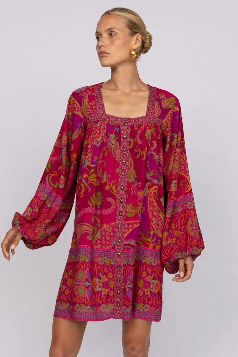 Woman wearing a vibrant pink patterned dress on a plain background