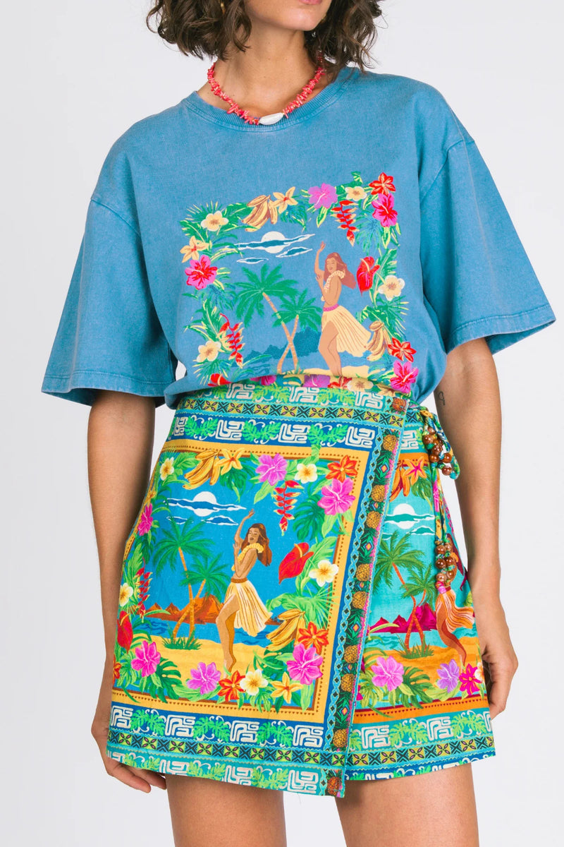 Person wearing a blue oversized shirt and colorful skirt with hula dancer design on a white background