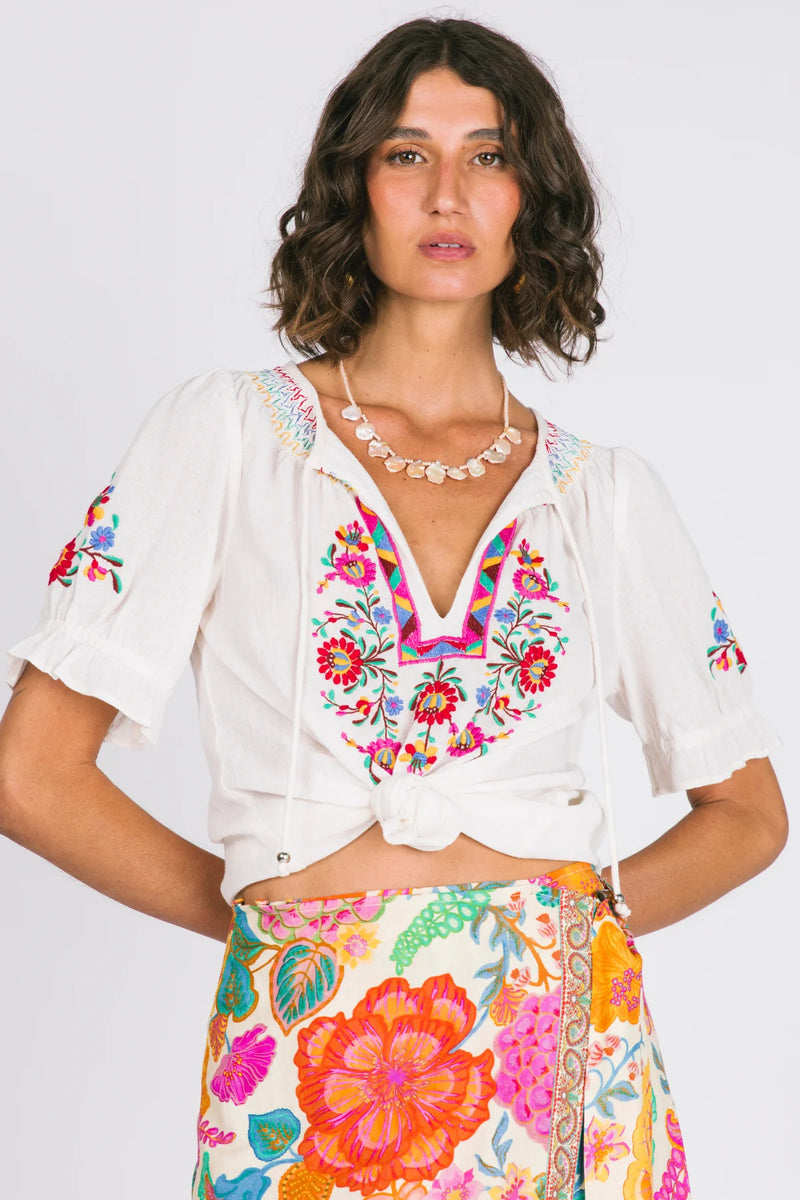 Woman wearing a white blouse with colorful embroidery and a floral skirt on a white background