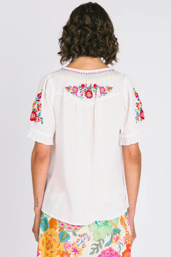 Woman wearing a white blouse with colorful floral embroidery on a plain background