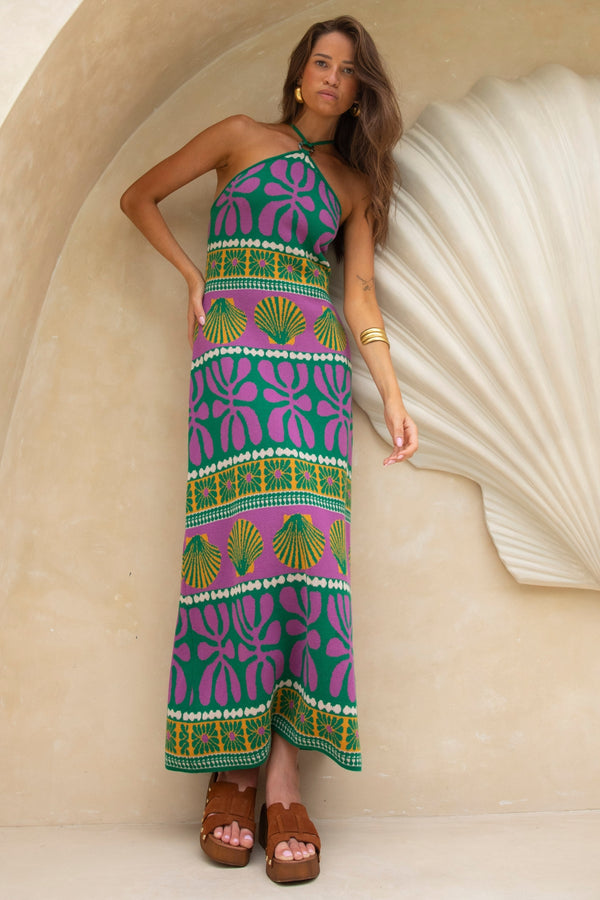 Woman wearing a colorful patterned dress standing against a beige wall.