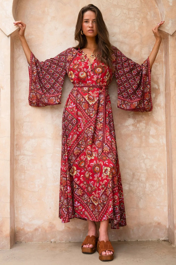 Woman in a red patterned dress standing in an arched stone hallway.