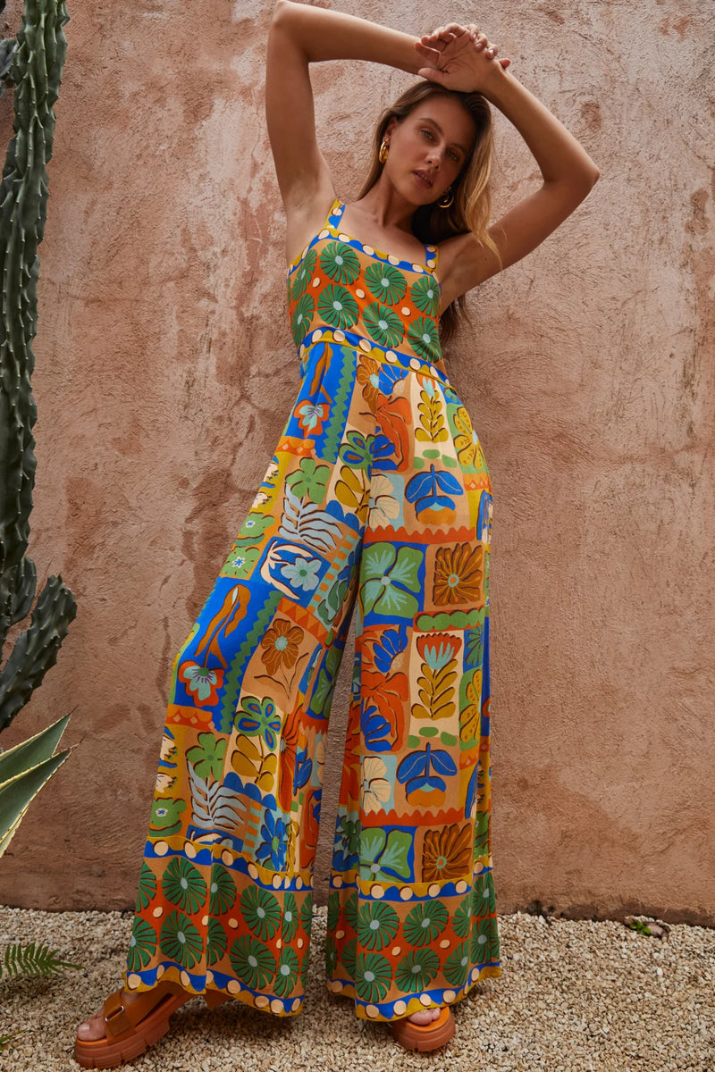 Woman wearing a colorful patterned jumpsuit against a textured wall.
