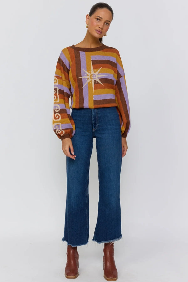 Person wearing a colorful sweater with abstract patterns and blue jeans on a white background