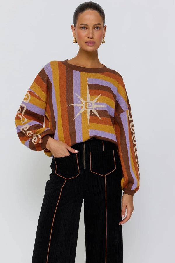 Person wearing a patterned sweater and black pants on a white background