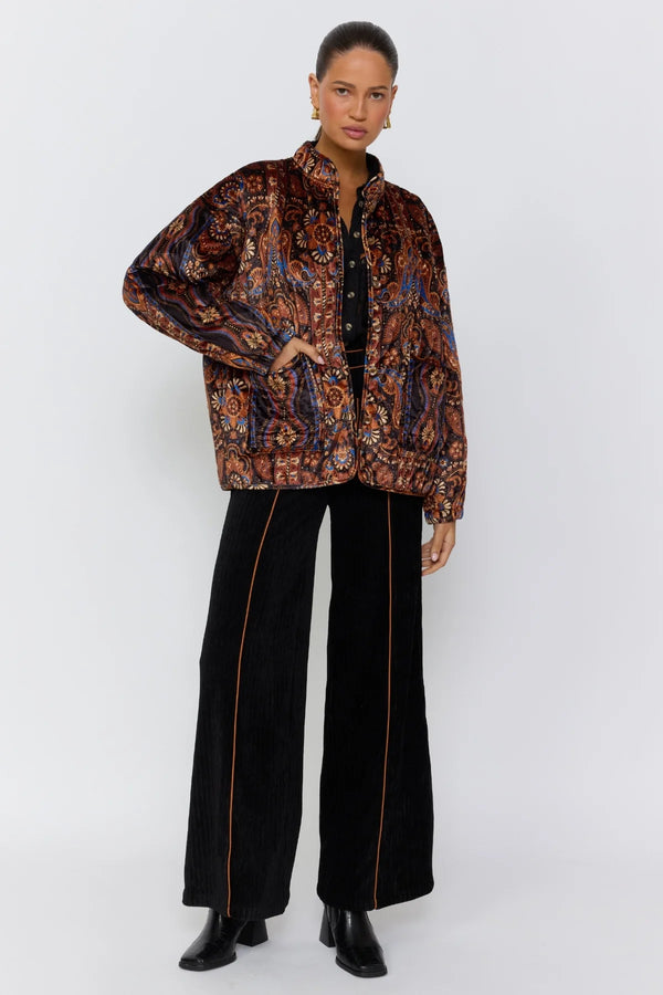Woman wearing a patterned jacket and black pants on a white background